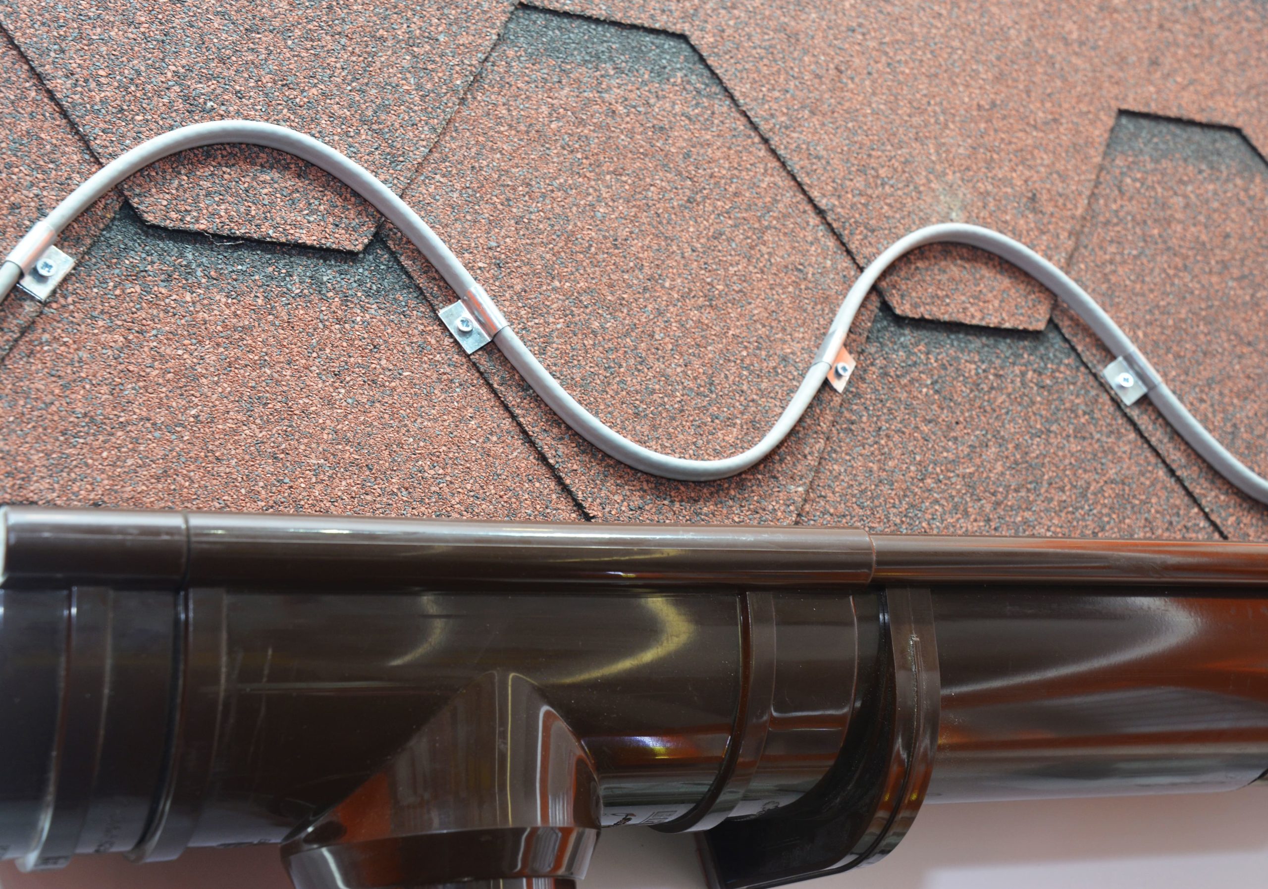Roofing heating cable for ice and snow melting. A close-up on a roofing deicing system, ice-melting cable installed above the rain gutter on an asphalt shingled roof